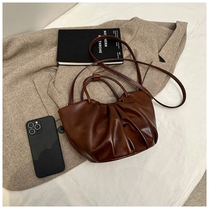 Detail of dark brown pleated cloud bag on khaki coat with lifestyle accessories