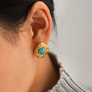 Close-up of a gold vintage textured earring with turquoise stone worn by a model