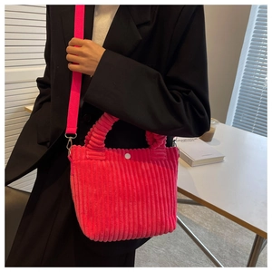 Detail of rose pink corduroy bucket bag with white button shown on a model's shoulder