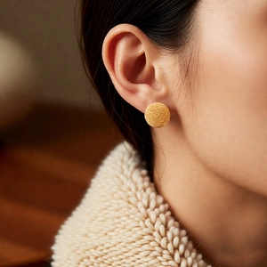 Close-up of golden round stud earrings with a brushed matte texture on model ear