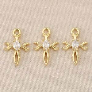 Detailed view of three 18K gold-plated baroque cross charms with oval clear zircon stones