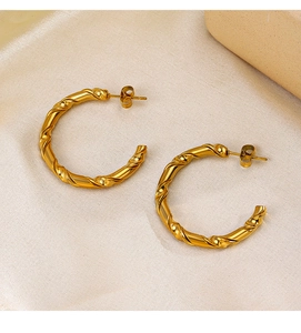 Detail of twisted 18K gold plated C-shape earrings on silk fabric with pebble decor