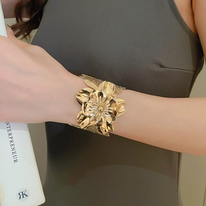 Close-up of golden wide-band cuff bracelet featuring a detailed layered floral design