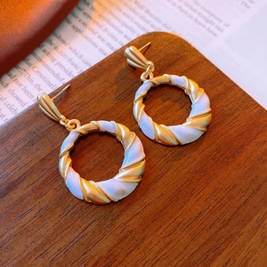 Close-up of vintage French twist hoop earrings with gold metal and white enamel textures