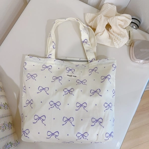 Detail of canvas tote bag with purple bow pattern and secure gray zipper closure