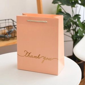 Detail of peach pink gift bag featuring golden Thank You text and woven handles