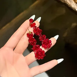 Boucles d'oreilles fleurs en cristal rouge foncé avec tiges dorées tenues à la main
