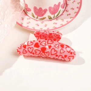 Pink heart pattern acrylic hair claw clip for women displayed on a floral plate