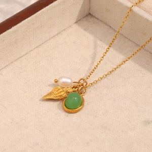 Close-up of 18K gold plated necklace with green gemstone, seashell, and pearl charms