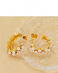 Detailed view of C-shaped gold pearl earrings with crystals on luxury satin background