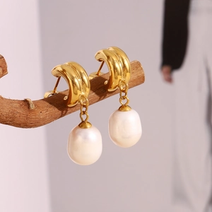 Detail of 18K gold-plated double arc earrings with drop-shaped baroque pearls on wood