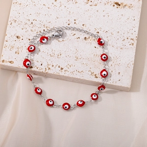 Detail of evil eye chain bracelet with red enamel beads on beige stone and satin background