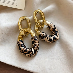 Detail view of geometric leopard print leather earrings on textured beige linen background
