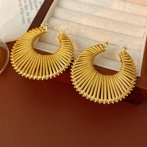 Detail shot of golden circular earrings with radial textured finish on beige velvet tray