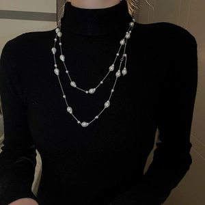 Detail of layered silver chain necklace with baroque pearls on a black turtleneck