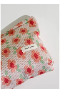 Close-up of pink knitted makeup bag with orange floral patterns and H&R BAG logo tag