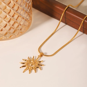 Golden sun pendant necklace with snake chain on elegant textured glass background
