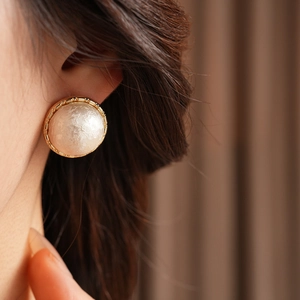 Close-up of a model wearing a gold textured round earring with a white pearl center
