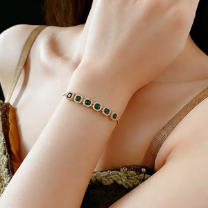 Gold bracelet with square emerald green stones and white zircon halo on female wrist