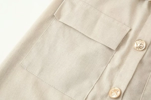 Dettaglio ravvicinato in misto lino beige con due bottoni dorati a rilievo e tasca