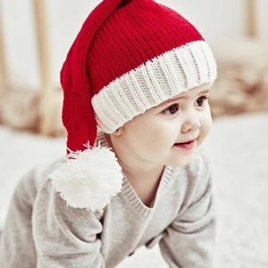 Detail of red and white baby winter knit hat with pom-poms on soft indoor background