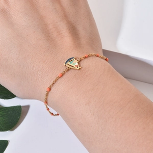 Golden stainless steel bracelet with sailboat charm and orange beads on wrist