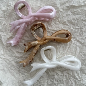 Three elegant bow-shaped marble hair claws in pink, amber, and white on textured paper