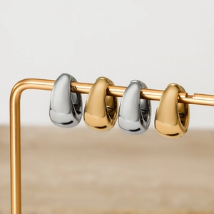 Minimalist thick teardrop huggie earrings in polished gold and silver on a display stand