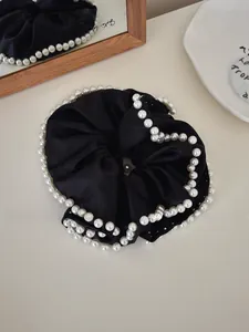 Detail of elegant black satin oversized scrunchie with white pearl trim on a white plate