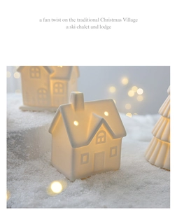 Close-up of matte white ceramic Christmas house with warm LED light on snowy background