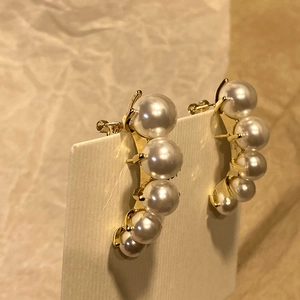 Detailaufnahme goldener Perlenohrringe mit fünf weißen Perlen in geschwungener Form