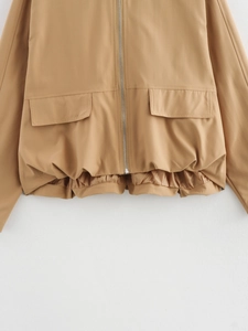 Detail of camel bomber jacket showing cargo pockets and elastic hem on a textured background