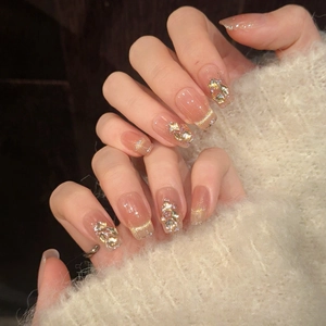 Detail of long square press-on nails with nude pink gradient and gold glitter tips
