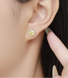 Close-up of sparkling round yellow gemstone stud earring with silver claw setting on ear