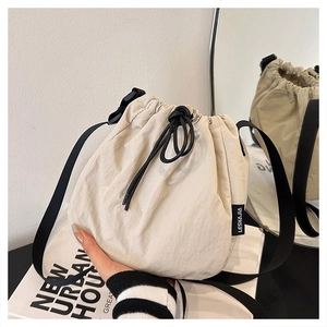 Detail shot of the cream nylon bucket bag with black drawstring closure and shoulder strap