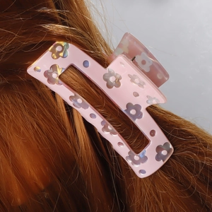 Pink floral hair claw clip with holographic petals worn on dark brown hair