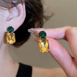 Detailed view of emerald green and champagne yellow crystal drop earrings on gold claw