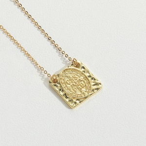 Close-up of golden Saint Benedict medal pendant with a hammered square base on white leather