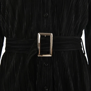 Close-up of black pleated shirt featuring a matching fabric belt and metallic buckle detail