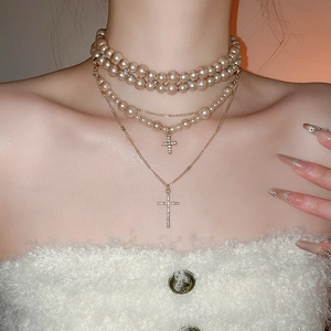 Macro shot of multi-layered pearl necklace featuring diamond-studded cross pendants