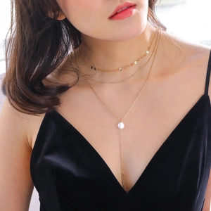Close-up of a layered gold necklace featuring a white pearl and a sleek metal bar pendant