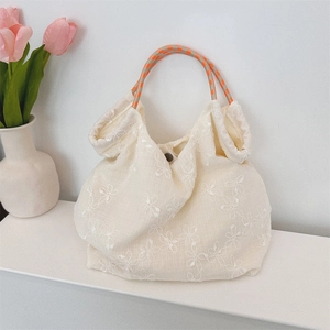 Detail of floral embroidery on cream canvas tote bag with woven rope handles
