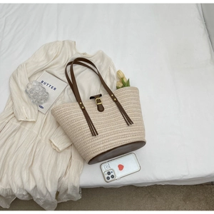 Detailed view of straw beach tote with dark brown leather straps and metal buckle closure
