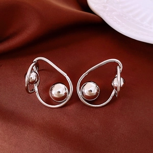 Détail macro de boucles d'oreilles boules en métal argenté sur tissu en soie rouge