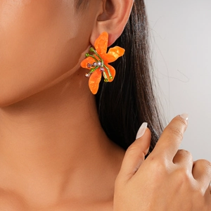 Resin flower earrings with orange petals and colorful beaded center on female model