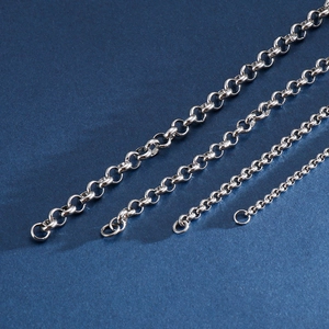 Detail of various thicknesses of polished silver rolo chains on a textured blue surface