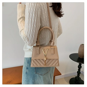 Detail view of apricot quilted PU leather handbag with gold V logo and tassel charm