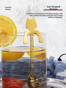 Golden cat-shaped stainless steel spoon hanging on a striped glass cup rim