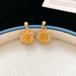 Detail of golden flower drop earrings with brushed metal texture in jewelry gift box