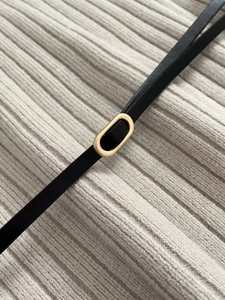 Detail of slim black leather belt with gold oval buckle on a beige knit sweater